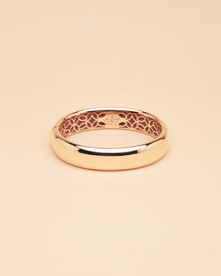 Gold bangle with intricate design on a beige background
