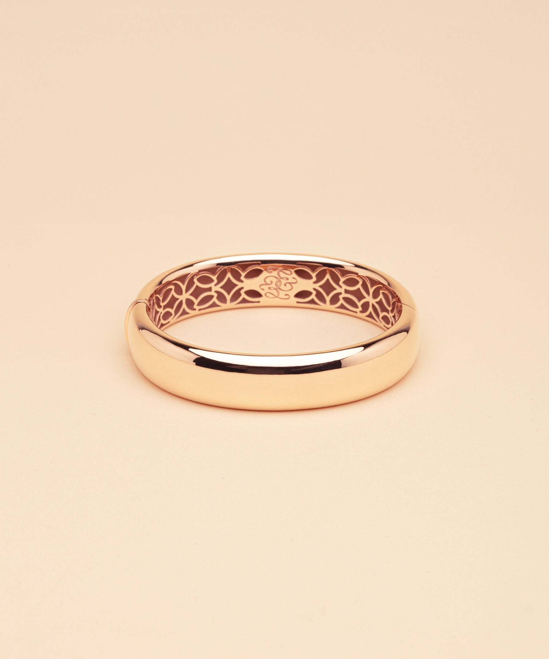 Gold bangle with intricate design on a beige background