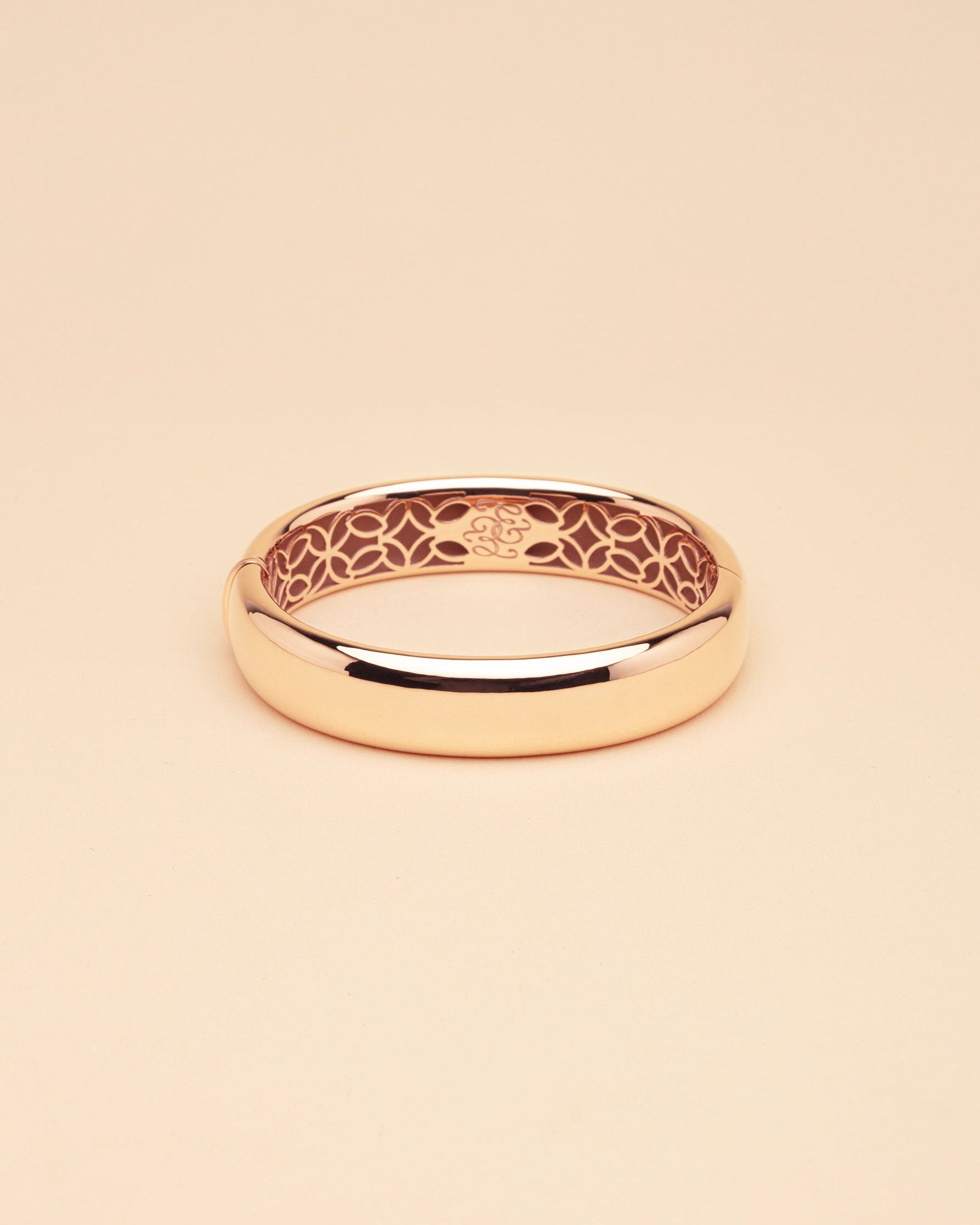 Gold bangle with intricate design on a beige background